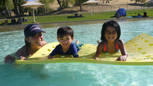 Salvavidas supervisando a dos niños en un gran flotador amarillo en la piscina