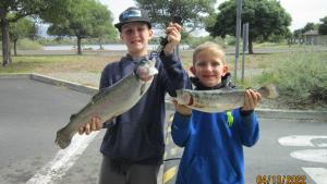 Two boys each holding a trout; they've caught.