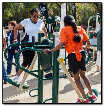 Two people using fitness equipment together - one in bright orange shirt, the other in a white shirt