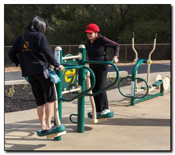Two people using fitness equipment together - one in sweatshirt and one with a red hat