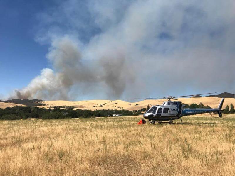 Helicoptor in grassy area with smoke in the background